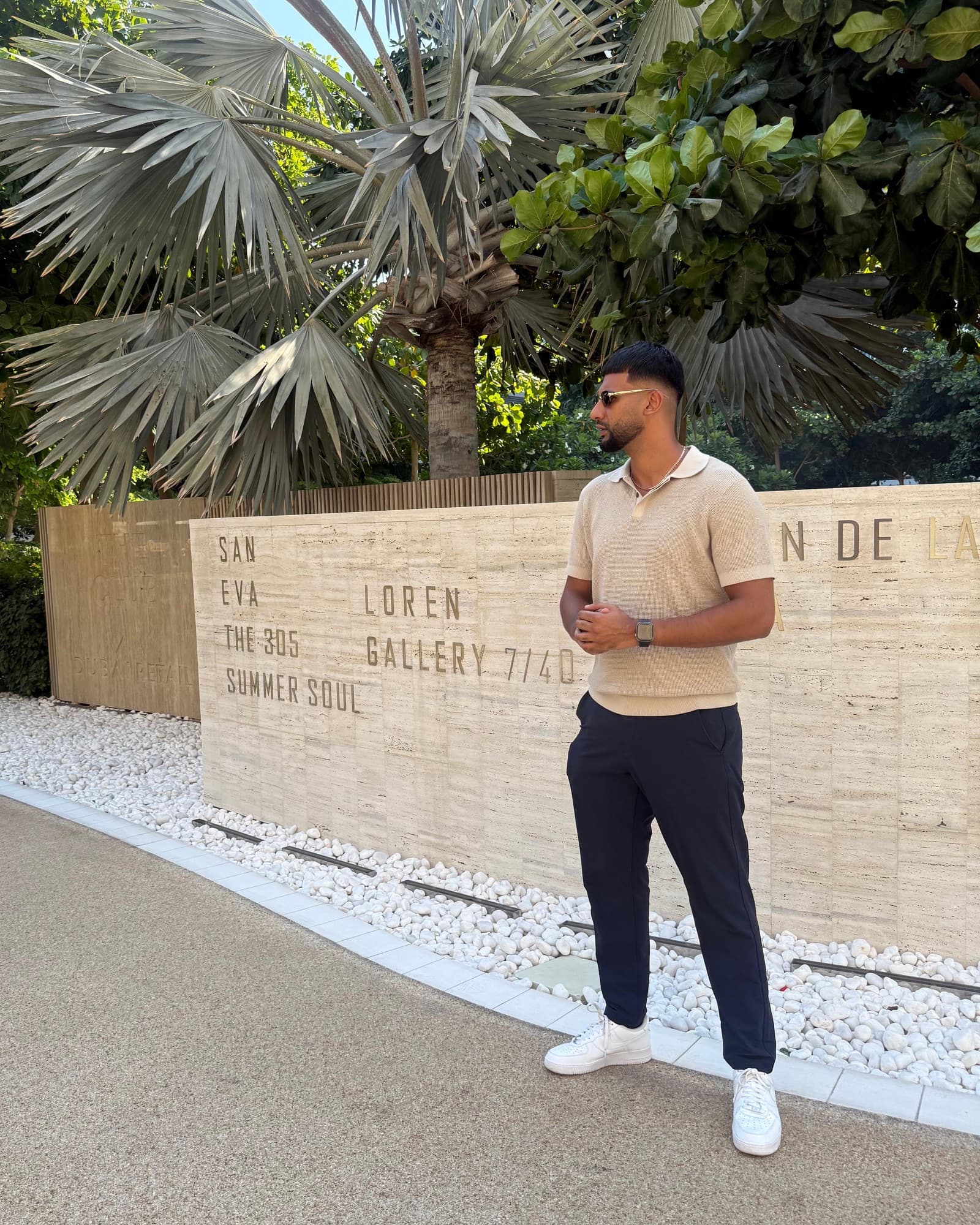 Niral Joshi standing outside, dressed smartly, in front of a stone wall and palm trees